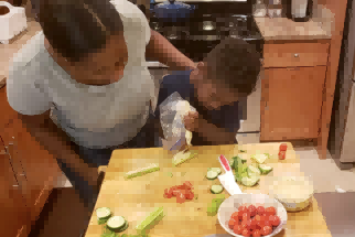 一对母子在制作 Wild Kratts 蜗牛食谱时将鹰嘴豆泥挤到芹菜杆上。