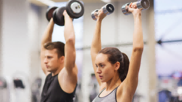男人和女人在健身房锻炼，将哑铃举过头顶